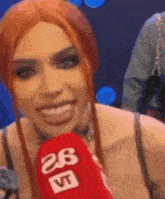 a woman with red hair is smiling while holding a red microphone that says 26 vt