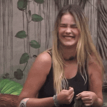a woman with long blonde hair wearing a black tank top laughs