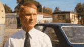 a man in a white shirt and black tie is standing in front of a car with a sign that says ya ke on it