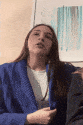 a woman wearing a blue sweater is sitting in front of a picture