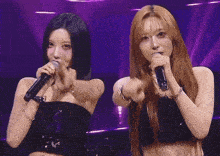 two women singing into microphones on a stage with purple background