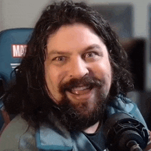a man with long hair and a beard is sitting in front of a microphone and smiling