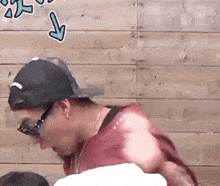 a man wearing glasses and a baseball cap is standing in front of a wooden wall with an arrow pointing down