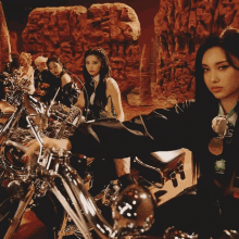 a group of women are sitting on motorcycles in front of a rock wall