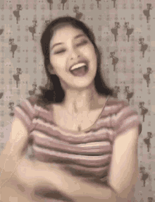 a woman in a pink striped shirt is laughing and making a funny face .