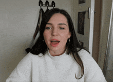 a woman wearing a white sweater and hoop earrings with her mouth open