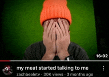 a man wearing an orange hat covering his face with his hands