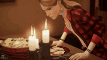a woman is sitting at a table with candles and a plate of food .