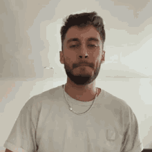 a man with a beard is wearing a white shirt and a silver chain around his neck
