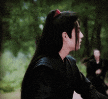 a man with long hair is wearing a black shirt and has a red ribbon in his hair .