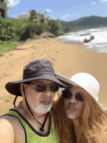 a man and woman wearing hats and sunglasses pose for a picture on the beach