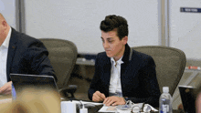 a woman in a suit sits at a table with a laptop
