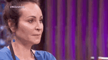 a woman wearing a blue shirt and earrings is sitting in front of a purple wall .