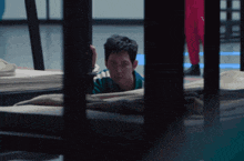 a man in a green and white shirt is looking out of a prison cell
