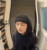a person wearing a hoodie and a beanie is standing in front of a door with their eyes closed .