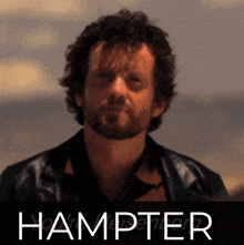 a man with a beard is standing in front of a poster that says hampter
