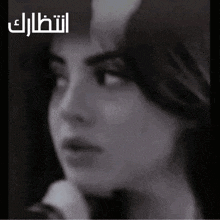 a woman 's face is shown in a black and white photo with arabic writing behind her