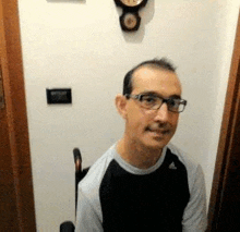 a man wearing glasses and a cane is sitting in a chair in front of a wall clock .