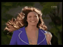 a woman in a purple jacket is smiling and her hair is blowing in the wind .
