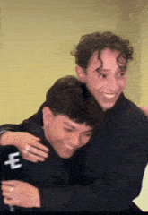 two young men are hugging each other and one has the letter e on his jacket