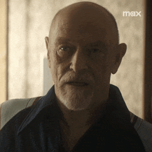 a man with a beard is sitting in front of a window with a max logo behind him
