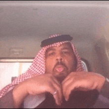 a man wearing a keffiyeh and a hat is sitting in a car and making a funny face .