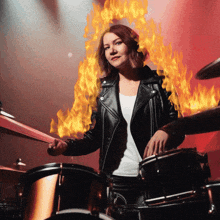 a woman in a leather jacket playing drums with flames coming out of her chest