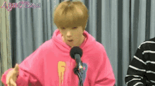 a young man in a pink hoodie is talking into a microphone .