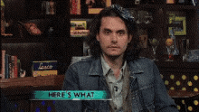 a man in a denim jacket is sitting in front of a bookshelf with the words here 's what below him