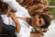 a young man in a white shirt is laying on a tree stump