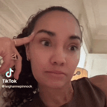 a woman with a ring on her finger is making a funny face while pointing at her eyebrow .