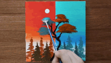 a person is painting a tree with a brush on a wooden table
