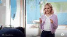 a woman is standing in a living room wearing a purple cardigan and a white shirt .