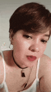 a woman with short hair is wearing a white tank top and a choker necklace
