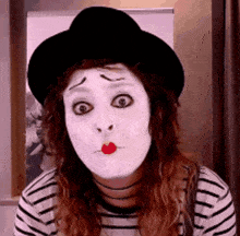 a woman wearing a mime mask and a black hat is making a funny face