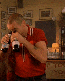 a man in a red shirt is drinking from two bottles of beer