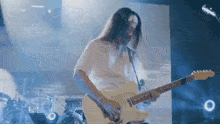 a man with long hair is playing an electric guitar on a stage .