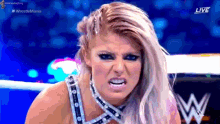 a woman is making a funny face while standing in a wrestling ring with a w logo in the background .