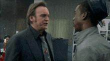 a man in a suit and tie talks to another man in a hat