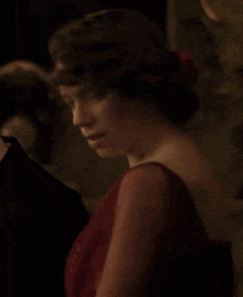 a woman in a red dress with a red headband looks at the camera