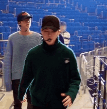 a man in a green sweater and a man in a blue sweater are walking in a stadium .