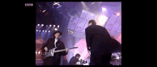 a man playing a guitar on a stage with bbc written in the corner