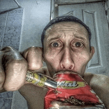 a man is holding a bag of potato chips in his mouth while drinking from a can .