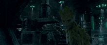 groot from guardians of the galaxy is standing in a dark room with a building in the background .