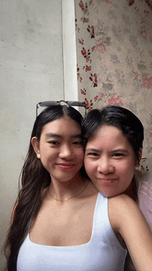 two girls are posing for a picture in front of a wall with flowers