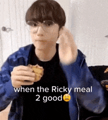 a young man wearing glasses and a blue jacket is eating a sandwich .