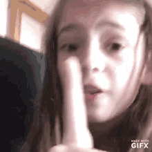 a young girl is making a funny face with her finger on her mouth .
