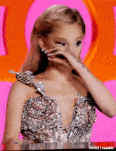a woman in a silver dress is covering her face with her hand .