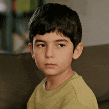 a young boy in a green shirt is looking at the camera