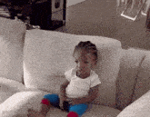 a baby is sitting on a white couch with a white shirt on